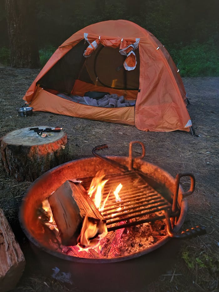 An inviting campsite featuring an orange tent and a warm fire pit under a twilight sky.