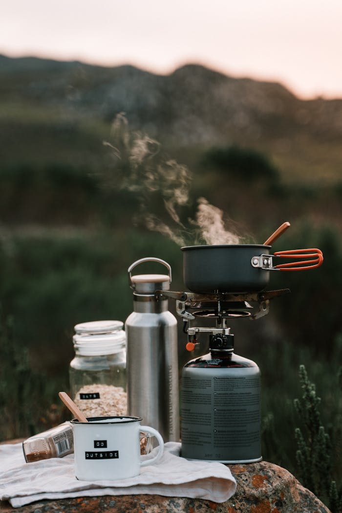 A picturesque outdoor camping scene with cooking gear and steam rising from a pot at sunrise.