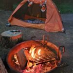 An inviting campsite featuring an orange tent and a warm fire pit under a twilight sky.